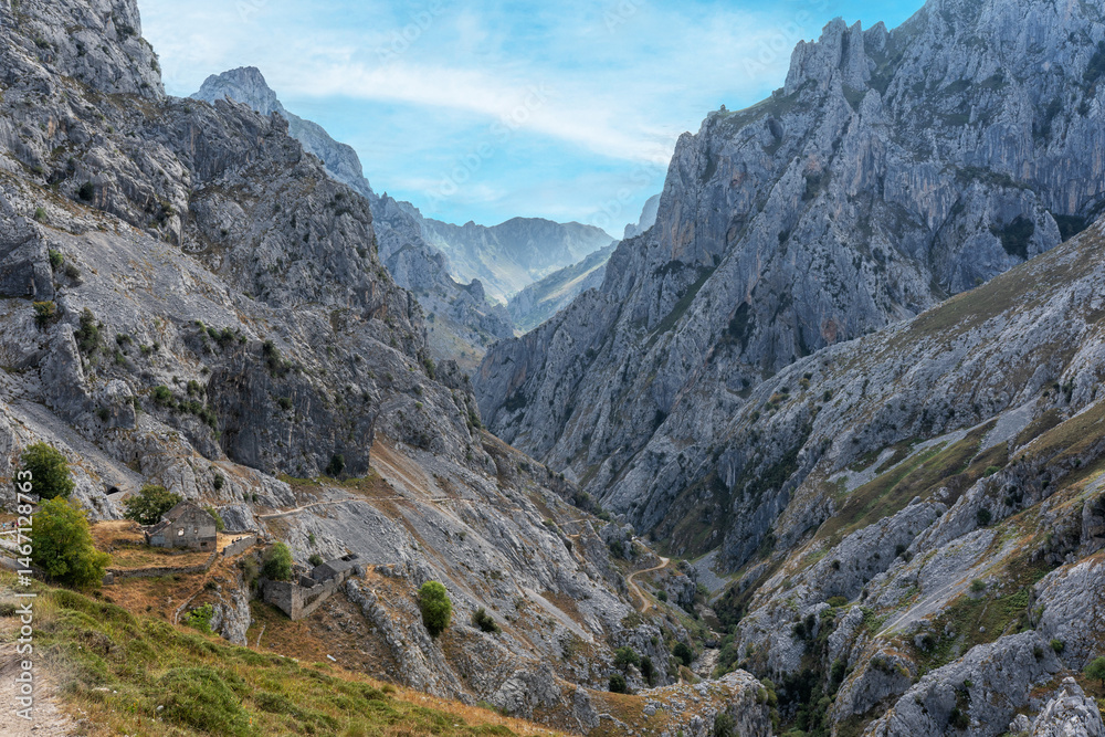 Fototapeta premium Stunning panoramic view of the dramatic rocky peaks and deep valleys of the Picos de Europa National Park in Spain, showcasing rugged cliffs, narrow gorges. Popular destination for hiking, adventure.