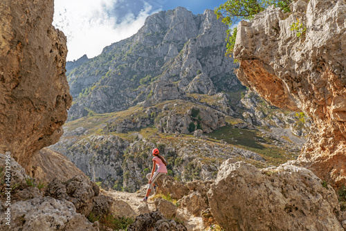 Young girl resting on a rocky mountain trail in the Picos de Europa, Spain. The Cares Trail (Ruta del Cares) features dramatic limestone cliffs, rugged terrain, and panoramic views.
