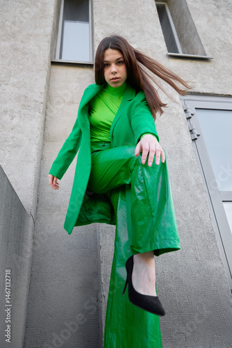 High fashion photo of a young brunette woman in green coat, poloneck and leather pants. photo