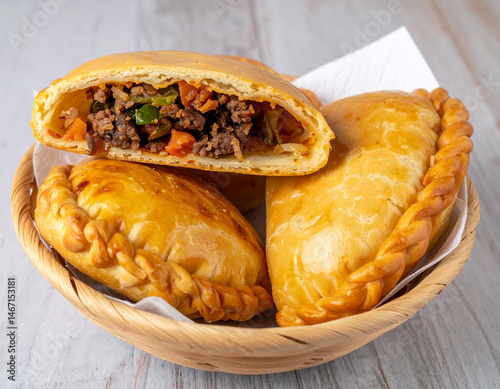 Fresh Salvadoran pastelitos filled with beef and vegetables served on a woven basket.