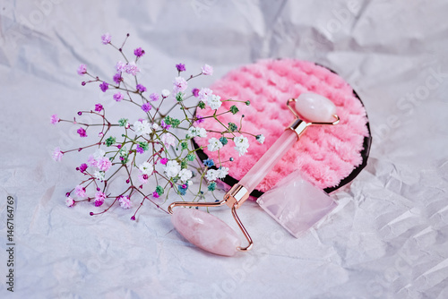 light cosmetic composition with a quartz roller, gypsophila, rose quartz crystal and a facial sponge on a crumpled paper background, creative focus
