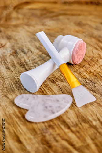 gua sha, silicone spatula for applying masks to the face and massage and cleaning brush on a wooden background