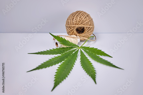 Close-up image of ball, spool of natural hemp fiber thread and hemp leaf on gray background, creative focus, organic eco-friendly fibers concept