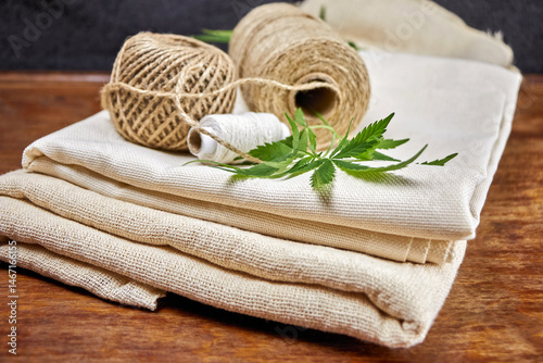 Close-up image of a green leaf, ball, skein, spool of natural hemp fiber thread on hemp fabric, creative focus, environmentally friendly natural resource concept