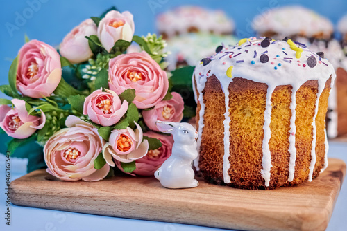 bright picture with the image of a small festive freshly baked paska, a flower bouquet and a cute bunny on a wooden board on a blue background close-up