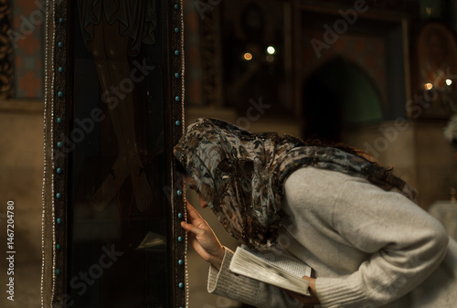 Quadro em tela Woman with Asian-European features in headscarf and white dress praying and lighting candles in an Orthodox church