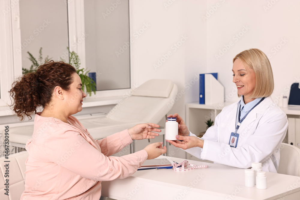 Fototapeta premium Weight loss. Smiling nutritionist giving medical bottle with pills to patient at table in clinic