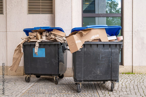 Überfüllte Altpapier-Tonnen mit Kartonabfällen vor einem Bürogebäude