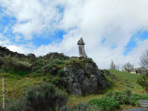 Statue of a hooded figure of Nazarene holding a torch on a rocky hill under a cloudy sky,