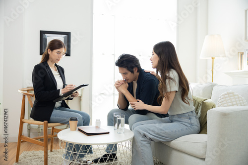 Stressed Asian man holding hands in worry while partner comforts beside, emotional tension from workplace failure, couple facing life challenge and considering professional mental health counseling