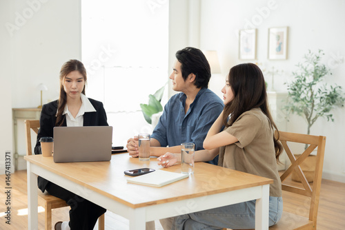 Asian couple sitting at table discussing property options with female real estate agent, showing trust, planning, and communication during home buying decision in relaxed lifestyle environment