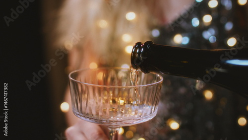 Women's hands hold round glasses, pour champagne. Women in a sparkling dress