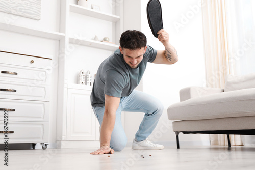 Billede på lærred Emotional young man killing cockroaches with slipper on floor indoors, low angle view