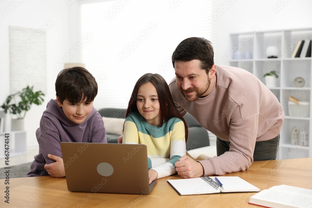 Father helping his kids with homework at wooden table indoors Father helping his kids with homework at wooden table indoors