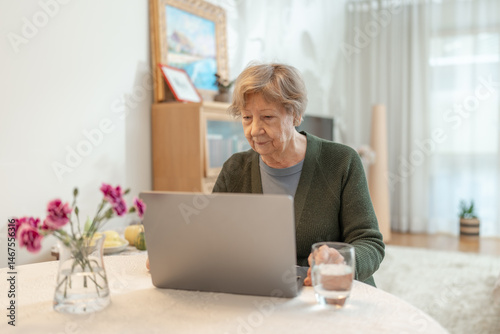 Senior woman using laptop at home, looking at the screen. Concept of technology, online shopping, digital literacy for seniors and active aging. Technology usage among seniors.