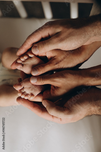 The central element of the image is the baby's legs, which are gently embraced by a man's and a woman's palms. A symbol of warmth, care, and family. 
