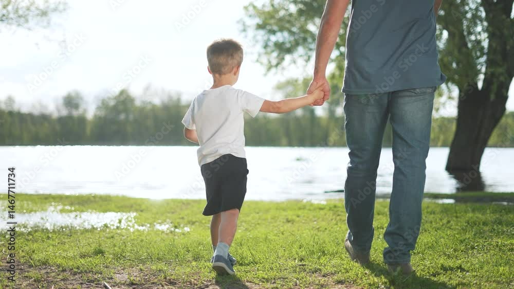 Happy Child holding father hand, walking together. Father and son bonding outdoors. Happy child and supportive father in park. Family enjoying nature walk together. Child feels support from parent.