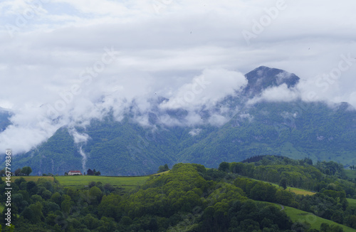 Obraz na płótnie Over the green mountain, the old farmhouse looked imposingly at the Txindoki, whose peak was sometimes hidden behind the clouds. w salonie