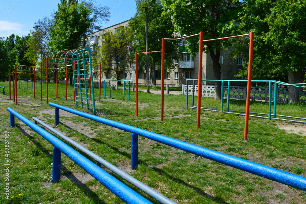 Outdoor workout playground with metal bars and climbing frames, old urban sports ground, sunny day, green grass, residential area. Outdoor workout playground with metal bars and climbing frames, old urban sports ground, sunny day, green grass, residential area.