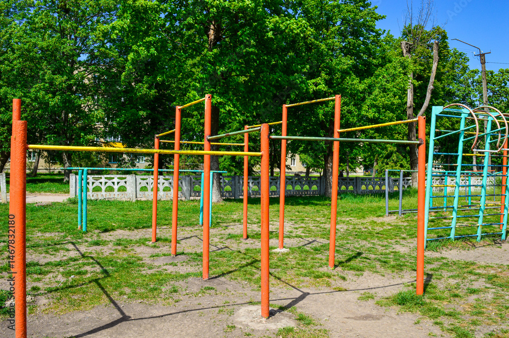 Outdoor workout playground with metal bars and climbing frames, old urban sports ground, sunny day, green grass, residential area. Outdoor workout playground with metal bars and climbing frames, old urban sports ground, sunny day, green grass, residential area.