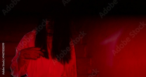 Horror scene of a mysterious Scary Asian ghost woman creepy have hair covering the face sitting on staircase at abandoned house with background dark red scene movie at night, holiday ghost Halloween