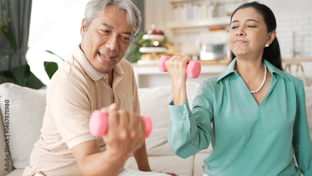 Fototapeta premium Happy elderly couple exercising together with dumbbells at home, focusing on muscle strength, joint health, and physical wellness for improved mobility and healthy aging. Retirement concept. Myrmidon.