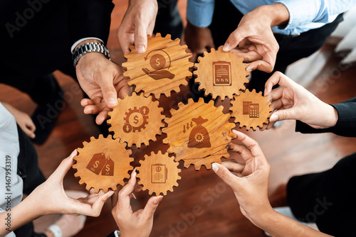 Hands gather around wooden gears displaying financial symbols, representing teamwork and collaboration in business growth and strategy development among professionals. Amity