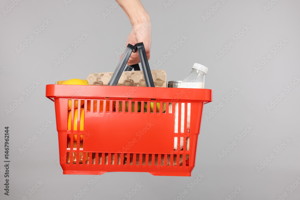 Fototapeta premium Man holding shopping basket with different products on grey background, closeup