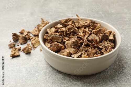 Pieces of dry chicory roots in bowl on gray textured table, closeup