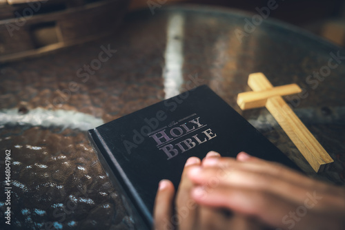 Close up Holy Bible on table, hands praying on book, light, hope, and salvation, symbol of Christian.