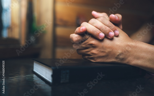 Close up of a man praying, hands clasped together on Bible, devotional concept.