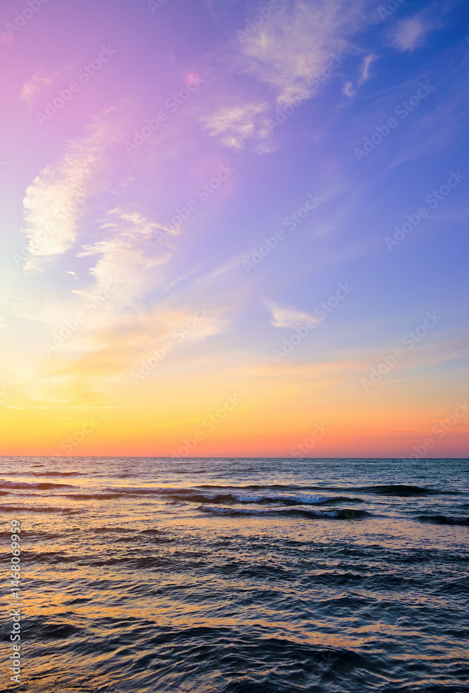 Fototapeta premium Colorful sunset over a calm sea with gentle waves and a vibrant sky. Serene ocean landscape perfect for travel, relaxation, or nature theme
