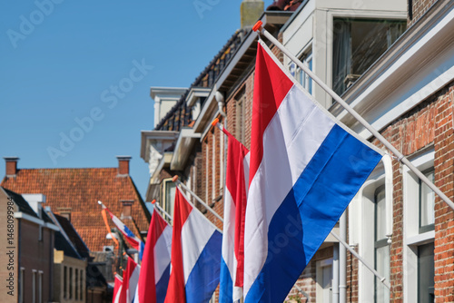 Dutch flags in a typical dutch street on Koningsdag under a blue sky. Koningsdag is a national holiday in the Kingdom of the Netherlands.	
