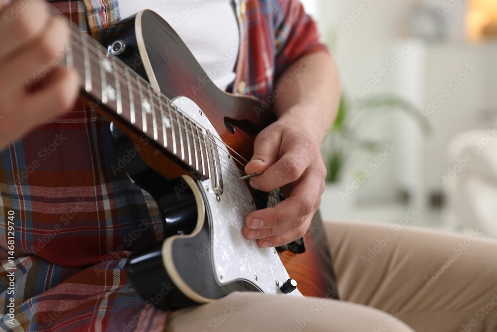 Fototapeta premium Man playing guitar with mediator at home, focus on hand