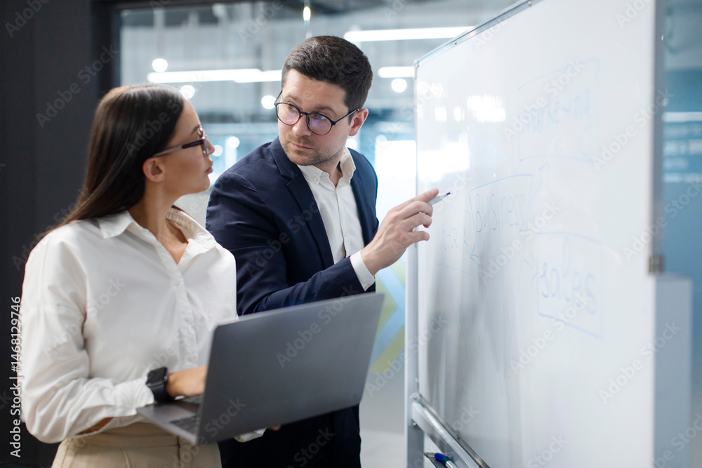 Naklejka premium Creative businessman and businesswoman meeting together in board room, thinking on new business ideas, standing near whiteboard with laptop