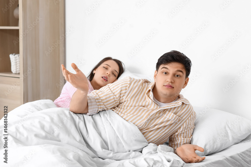 Fototapeta premium Young annoyed man lying in bed with his snoring wife at home