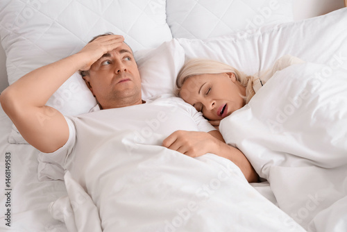 Mature man cannot sleep because of his wife's snoring in bedroom