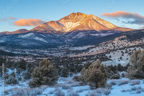 Snow covered mountain peaks glowing golden sunlight with a clear blue sky and soft clouds below