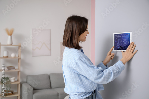 Foto Young happy woman using smart home security system control panel on wall in room