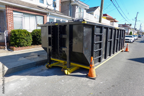 Black dumpster on a street in front of an old house