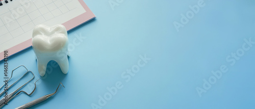 Dental tooth model with stainless steel dental tools and monthly calendar on blue background. Oral health care appointment reminder concept.