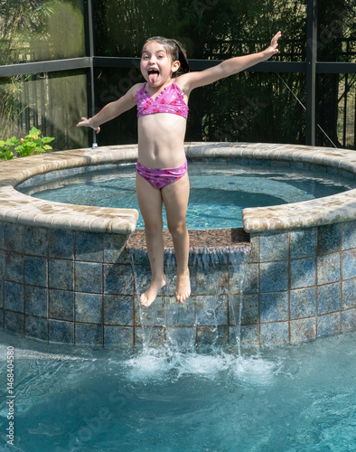A young girl leaping into a swimming pool with a joyful expression on her face