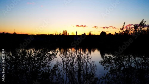 A distant church stands silhouetted by the setting sun as a river flows in the foreground. A peaceful blend of spiritual presence and natural beauty.


