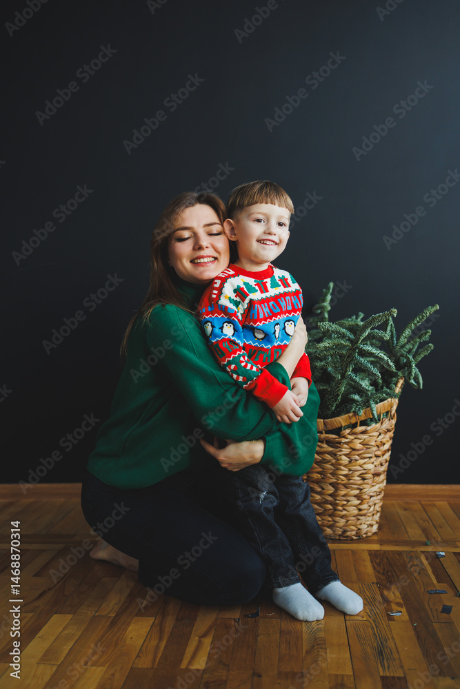 Mother and little son at home on Christmas, child smiles at mother, congratulates and gives unexpected gift. Woman mother receives gift from son on birthday. Family holiday, love concept