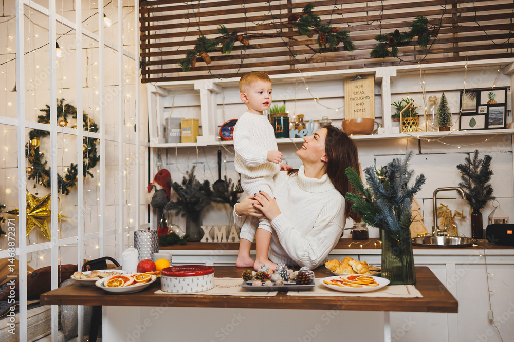 Mother and little son at home on Christmas, child smiles at mother, congratulates and gives unexpected gift. Woman mother receives gift from son on birthday. Family holiday, love concept