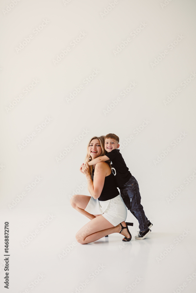 Cute mother and baby boy hugging while sitting on white background. Happy mother and baby son waiting for dad to return from work. Fun games of mother and son.