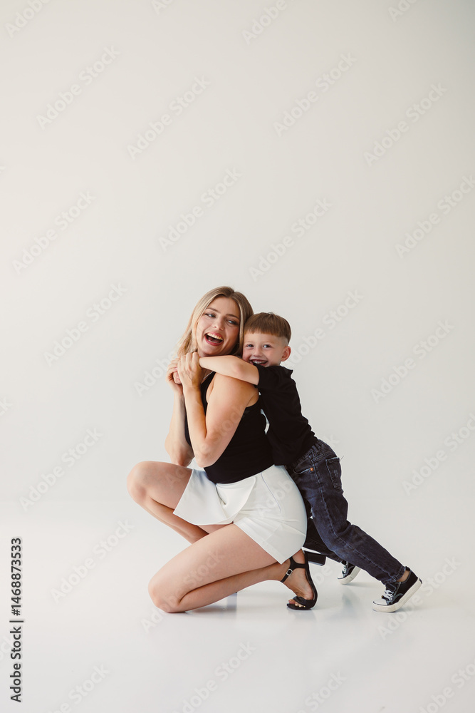 Cute mother and baby boy hugging while sitting on white background. Happy mother and baby son waiting for dad to return from work. Fun games of mother and son.