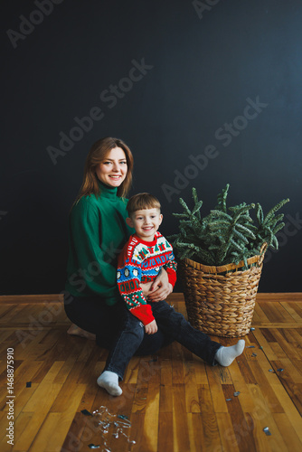 Obraz na płótnie Mother and little son at home on Christmas, child smiles at mother, congratulates and gives unexpected gift. Woman mother receives gift from son on birthday. Family holiday, love concept w salonie
