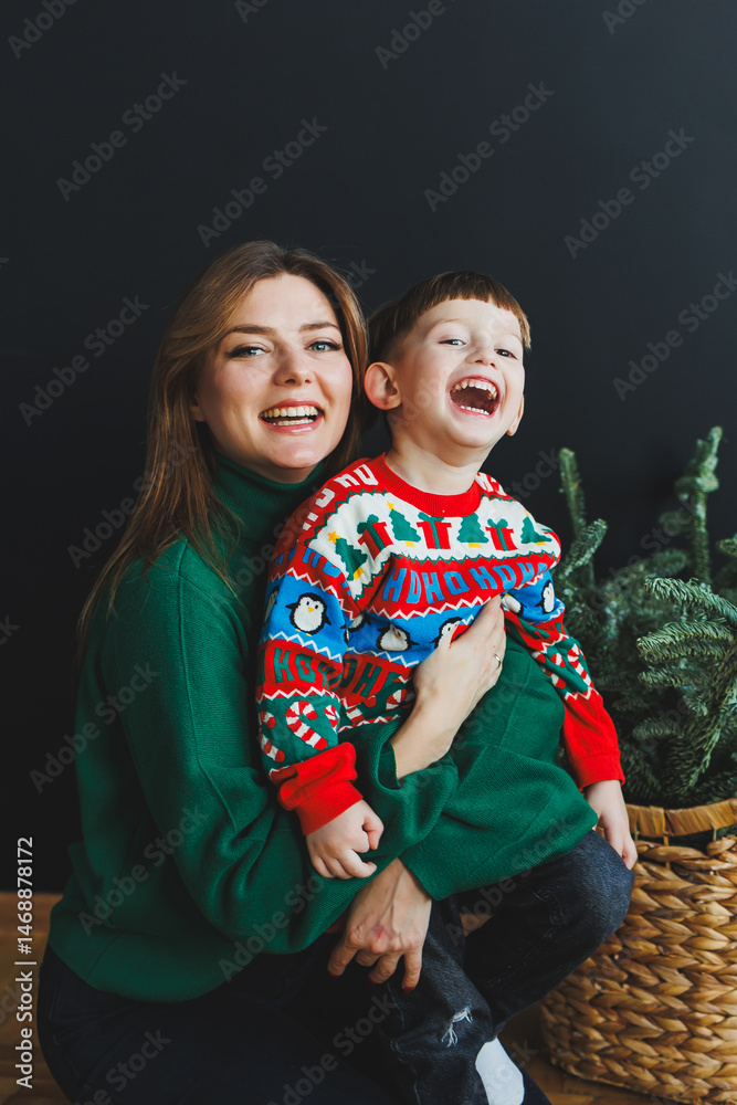 Mother and little son at home on Christmas, child smiles at mother, congratulates and gives unexpected gift. Woman mother receives gift from son on birthday. Family holiday, love concept