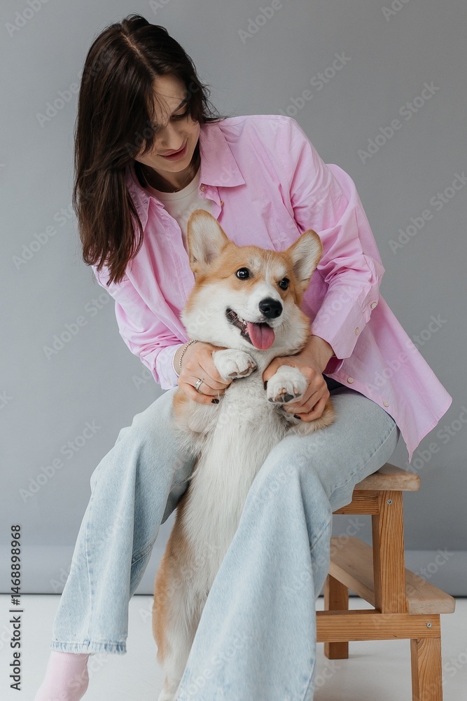 Happy brunette sitting next to corgi dog indoors. Cheerful girl in good mood stroking animal. Concept of friendship between man and pet.
